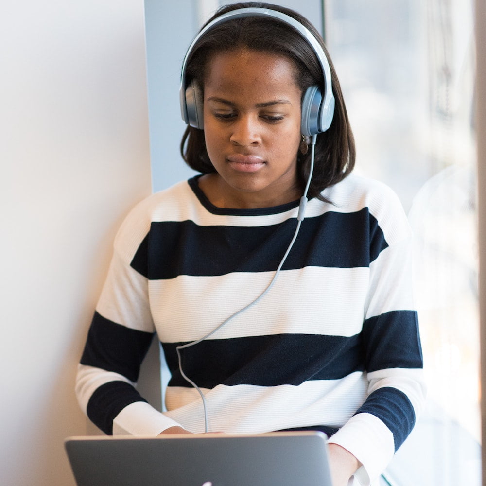 A young woman with headphones on listening to a laptop